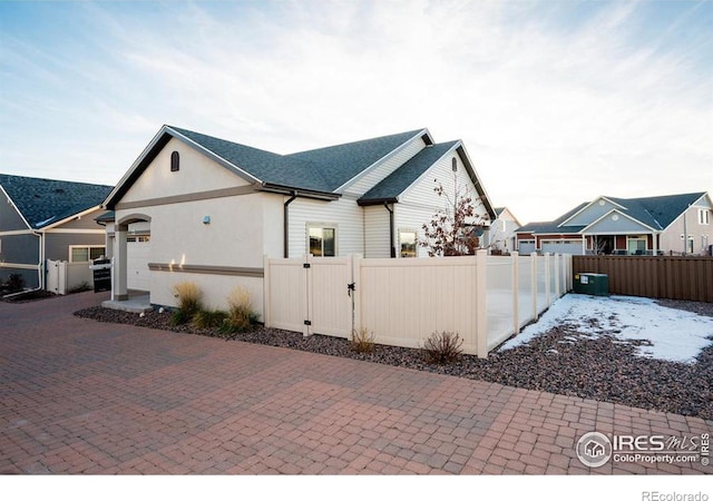 view of side of property with a garage, a shingled roof, a fenced front yard, a gate, and decorative driveway