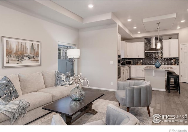 living area featuring a tray ceiling, baseboards, recessed lighting, and wood finished floors