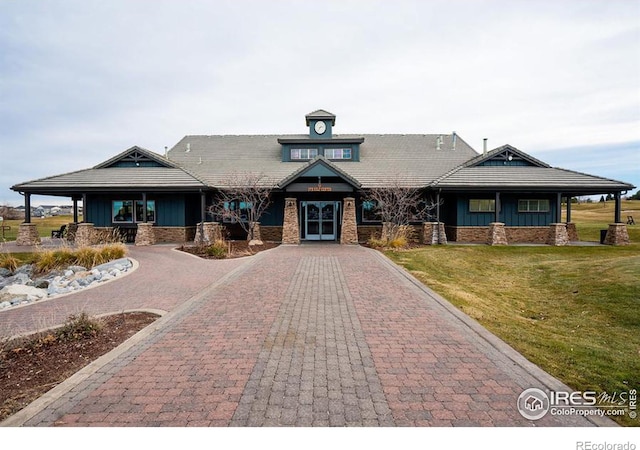 view of front of house featuring board and batten siding, decorative driveway, brick siding, and a front lawn