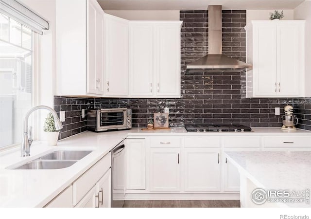 kitchen with black gas stovetop, a toaster, a sink, white cabinetry, and wall chimney exhaust hood