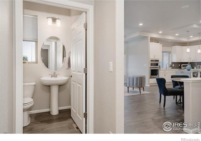 bathroom featuring decorative backsplash, wood finished floors, toilet, and a healthy amount of sunlight