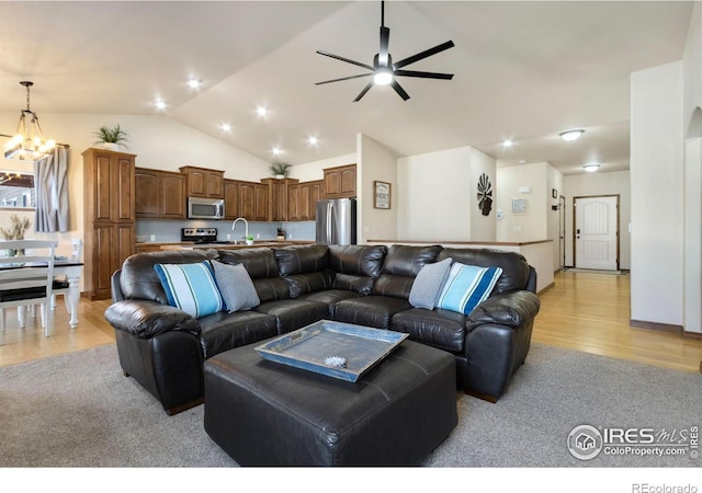 living room featuring ceiling fan with notable chandelier, light hardwood / wood-style floors, lofted ceiling, and sink