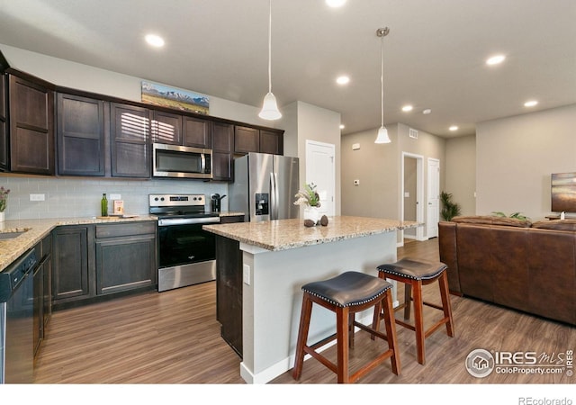 kitchen with tasteful backsplash, a center island, hanging light fixtures, light hardwood / wood-style flooring, and appliances with stainless steel finishes