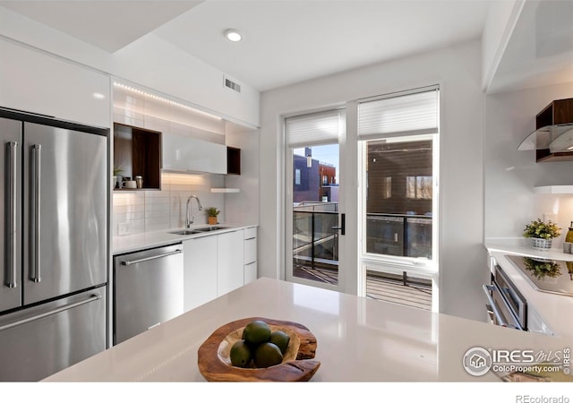 kitchen with backsplash, stainless steel appliances, white cabinetry, and sink