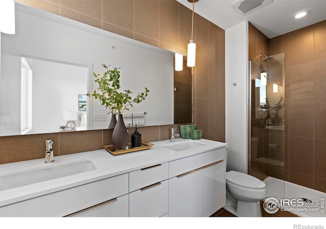 bathroom with a tile shower, backsplash, toilet, vanity, and tile walls