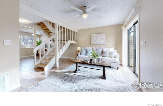 living room with ceiling fan, plenty of natural light, a textured ceiling, and light wood-type flooring