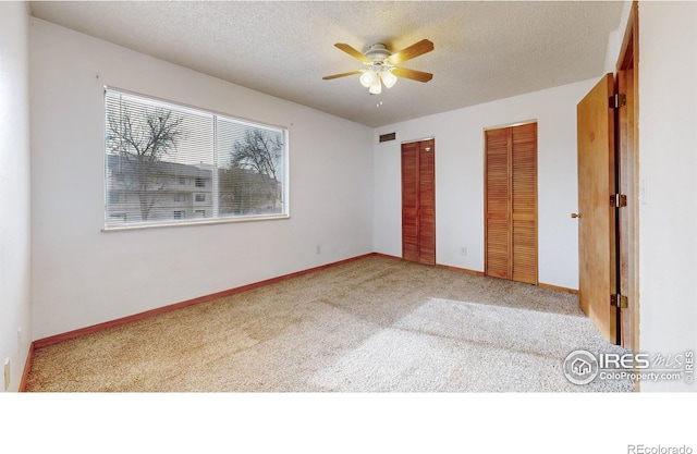 unfurnished bedroom with a textured ceiling, ceiling fan, light colored carpet, and two closets