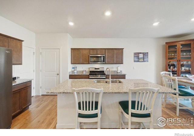 kitchen featuring light stone countertops, appliances with stainless steel finishes, sink, light hardwood / wood-style flooring, and an island with sink