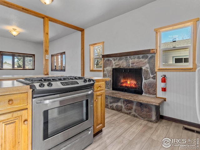 kitchen featuring plenty of natural light, stainless steel range with gas cooktop, a fireplace, and light hardwood / wood-style flooring