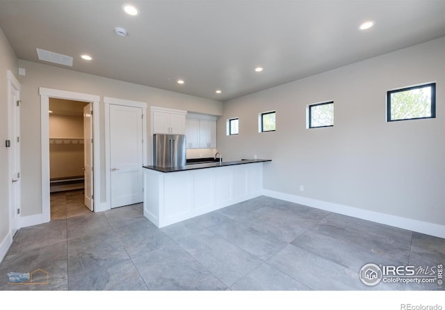 kitchen with high quality fridge, a peninsula, white cabinetry, baseboard heating, and dark countertops