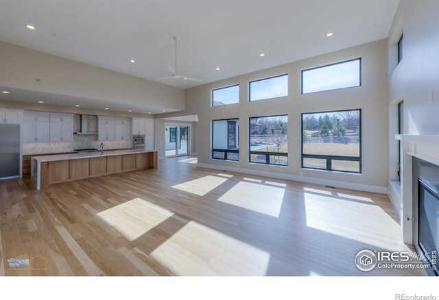 unfurnished living room with light wood-type flooring, a glass covered fireplace, a towering ceiling, and recessed lighting