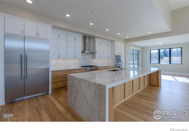 kitchen with stainless steel appliances, a spacious island, white cabinets, a sink, and wall chimney exhaust hood