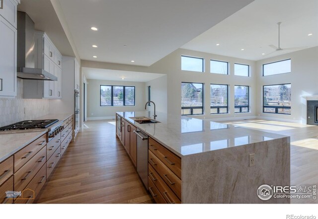 kitchen featuring a spacious island, wall chimney exhaust hood, open floor plan, white cabinetry, and a sink