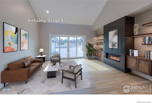 living room featuring a large fireplace, high vaulted ceiling, and light wood-style floors