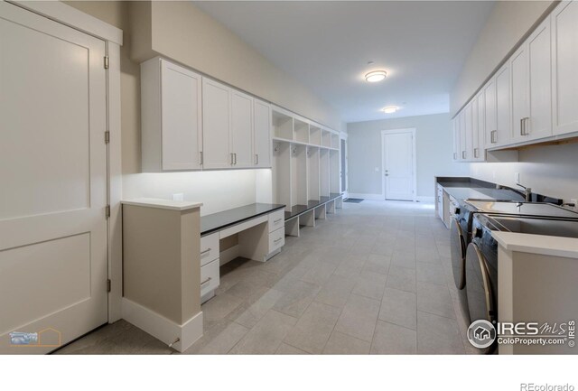 kitchen featuring built in desk, white cabinets, washer and clothes dryer, and baseboards