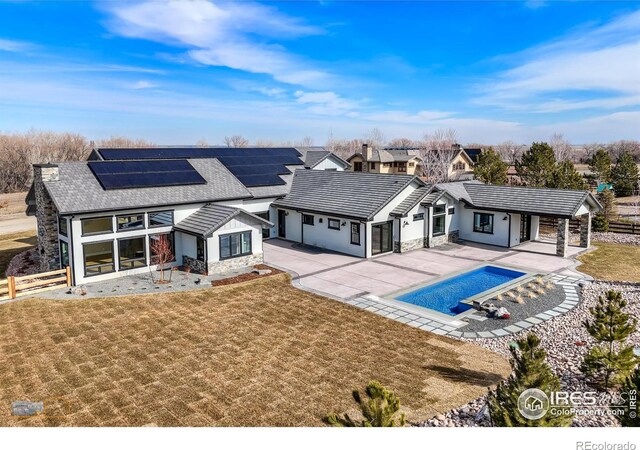 back of property with a yard, a covered pool, fence, and roof mounted solar panels