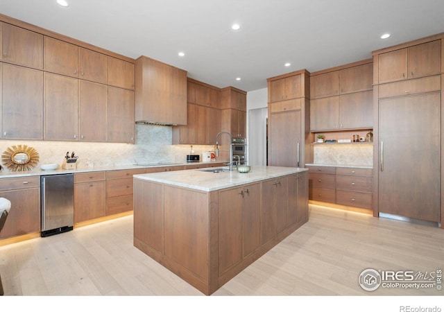 kitchen featuring a center island with sink, sink, light hardwood / wood-style flooring, decorative backsplash, and appliances with stainless steel finishes