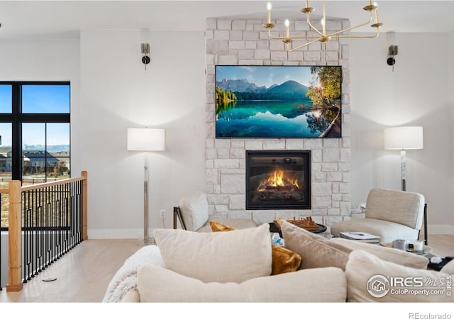 living room featuring a stone fireplace, light hardwood / wood-style floors, and an inviting chandelier