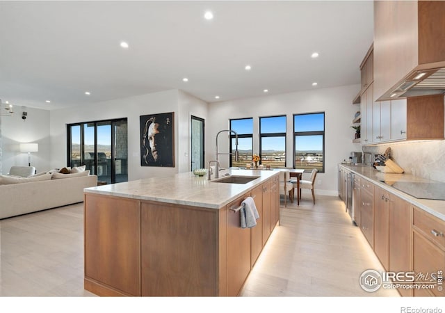 1722 Fire Glow Dr, Windsor, CO 80550 - kitchen featuring premium range hood, black electric cooktop, light wood finished floors, an island with sink, and plenty of natural light