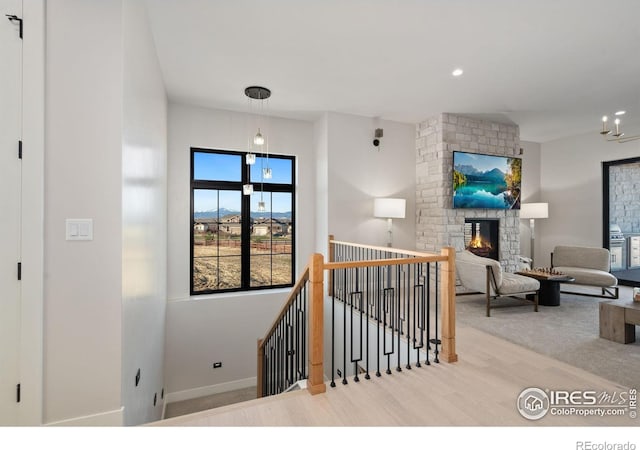 stairway with hardwood / wood-style floors, a stone fireplace, and a chandelier