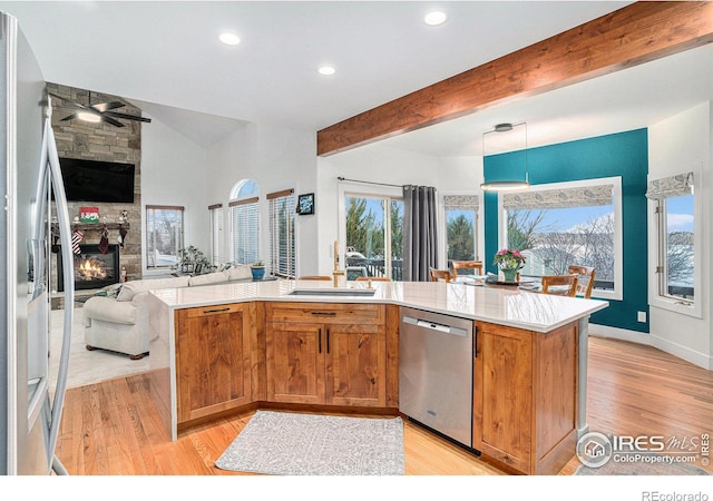 kitchen with a stone fireplace, light wood-type flooring, hanging light fixtures, and appliances with stainless steel finishes