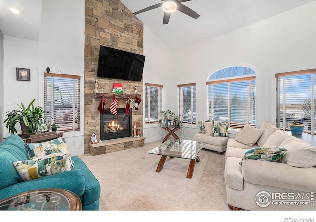 living room with ceiling fan, a stone fireplace, light colored carpet, and high vaulted ceiling