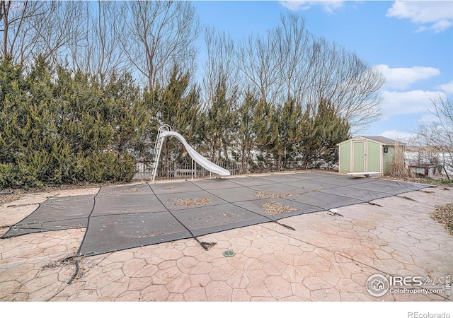 view of pool featuring a storage unit, a diving board, a patio area, and a water slide