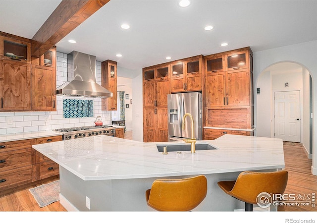 kitchen featuring wall chimney range hood, backsplash, a spacious island, appliances with stainless steel finishes, and light wood-type flooring