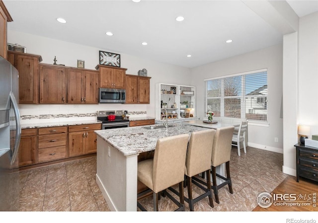 kitchen with light stone countertops, sink, stainless steel appliances, a kitchen bar, and a kitchen island with sink