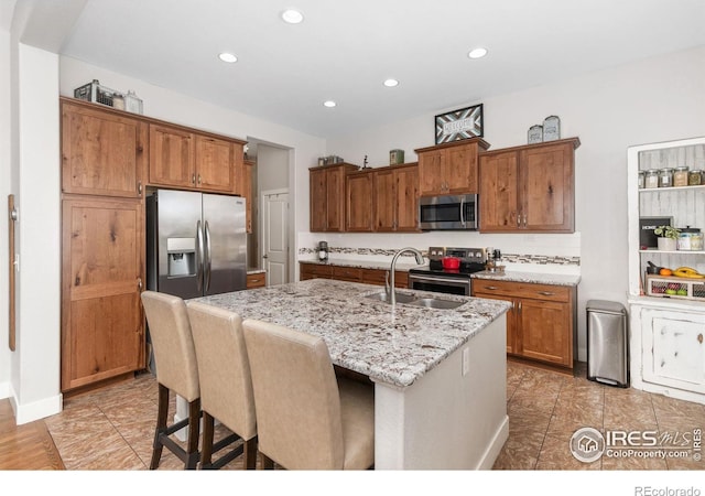 kitchen featuring light stone countertops, sink, stainless steel appliances, a kitchen bar, and a kitchen island with sink