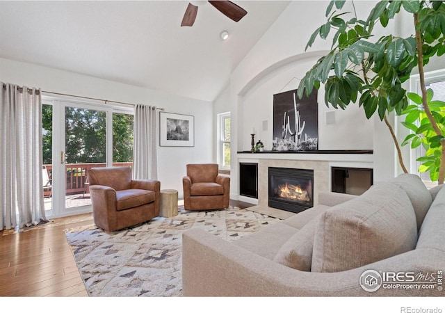 living room with hardwood / wood-style flooring, high vaulted ceiling, ceiling fan, and a tiled fireplace