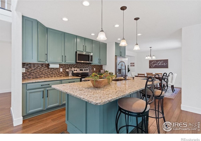 kitchen with hanging light fixtures, stainless steel appliances, light wood-type flooring, and sink