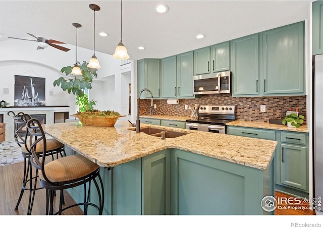 kitchen featuring green cabinets, sink, stainless steel appliances, and an island with sink