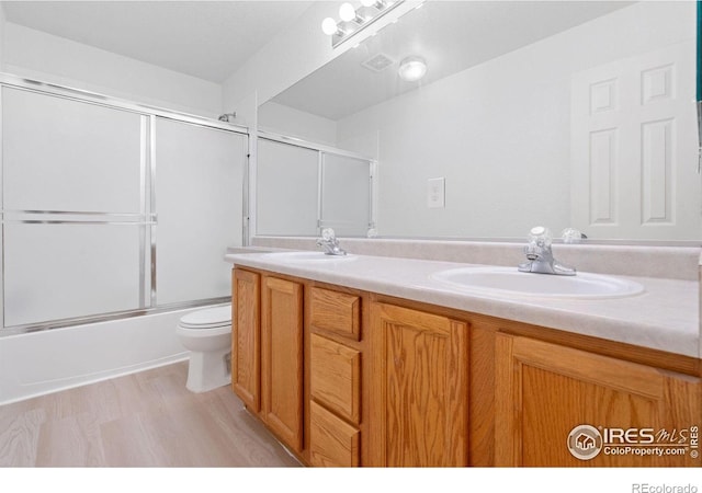 full bathroom with hardwood / wood-style flooring, vanity, toilet, and enclosed tub / shower combo