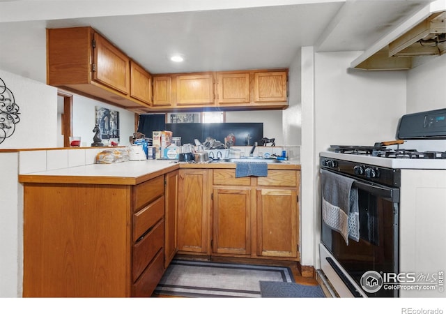 kitchen featuring kitchen peninsula, ventilation hood, and white gas range