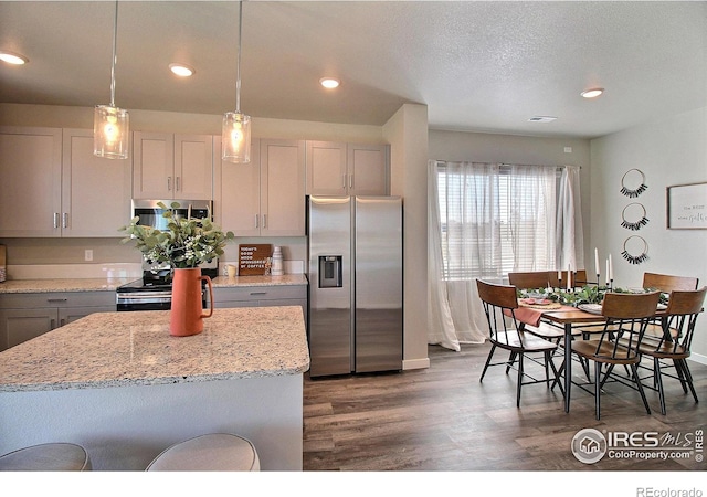 kitchen with light stone counters, appliances with stainless steel finishes, dark hardwood / wood-style floors, gray cabinets, and a kitchen island