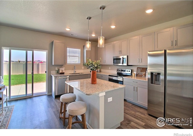 kitchen featuring sink, decorative light fixtures, a center island, appliances with stainless steel finishes, and light stone countertops