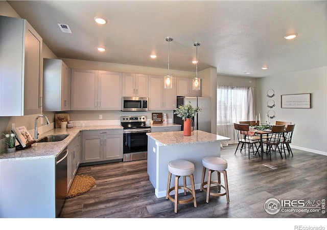 kitchen with a kitchen island, decorative light fixtures, sink, dark hardwood / wood-style flooring, and stainless steel appliances