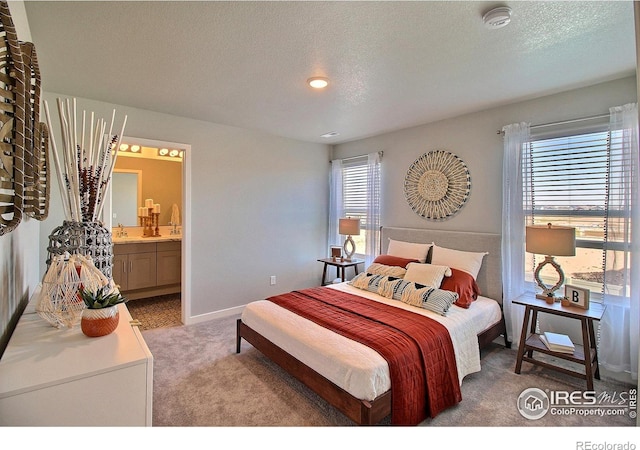 bedroom with light colored carpet, ensuite bath, sink, and a textured ceiling