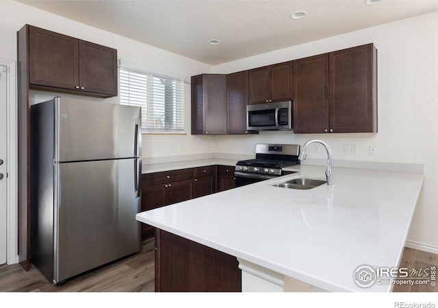 kitchen featuring kitchen peninsula, appliances with stainless steel finishes, dark brown cabinets, sink, and wood-type flooring