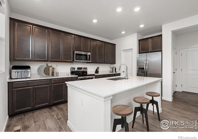 kitchen featuring a breakfast bar, a center island with sink, sink, hardwood / wood-style flooring, and stainless steel appliances