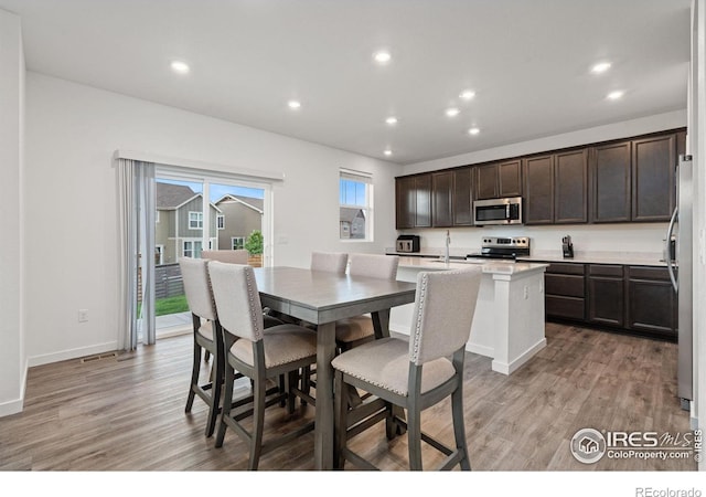 kitchen with a center island with sink, stainless steel appliances, dark brown cabinets, and light wood-type flooring