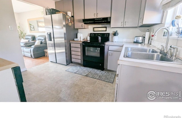 kitchen featuring black electric range oven, sink, stainless steel fridge, gray cabinets, and light wood-type flooring