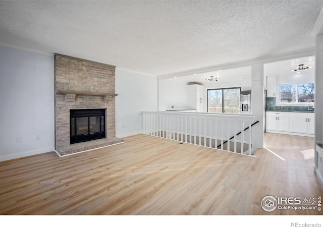 unfurnished living room with a textured ceiling, a brick fireplace, a notable chandelier, and light wood-type flooring