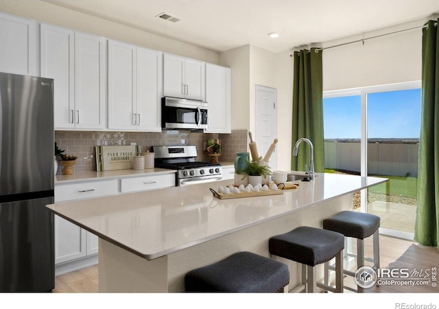 kitchen with tasteful backsplash, appliances with stainless steel finishes, a kitchen island with sink, and white cabinets