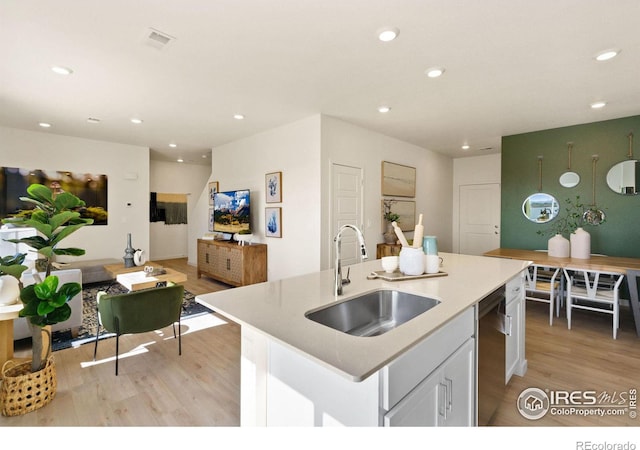 kitchen featuring sink, white cabinetry, light wood-type flooring, dishwasher, and an island with sink