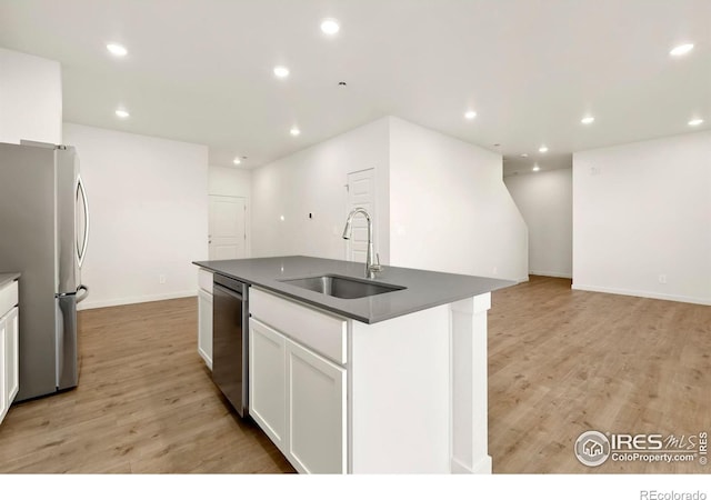 3218 Buffalo Grass Ln, Wellington, CO 80549 - kitchen with stainless steel appliances, a sink, dark countertops, light wood-style flooring, and a kitchen island with sink