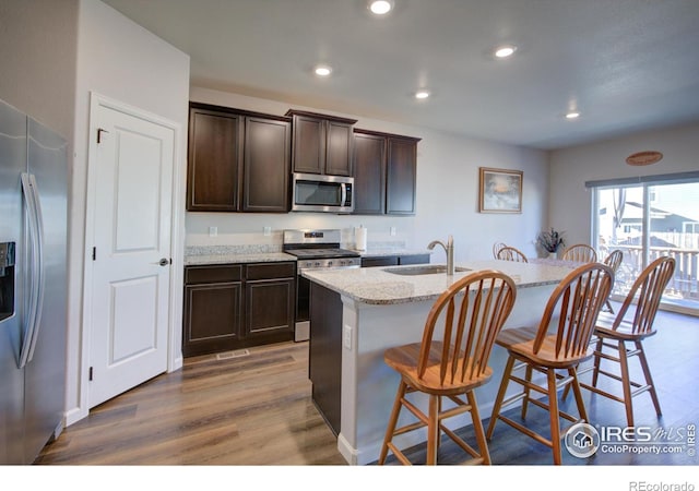 kitchen featuring light stone countertops, appliances with stainless steel finishes, sink, a center island with sink, and light hardwood / wood-style floors