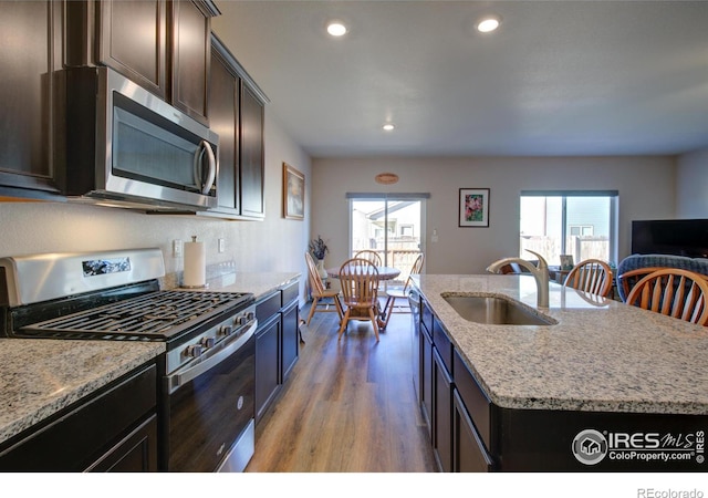 kitchen featuring a center island with sink, sink, light hardwood / wood-style flooring, light stone countertops, and appliances with stainless steel finishes