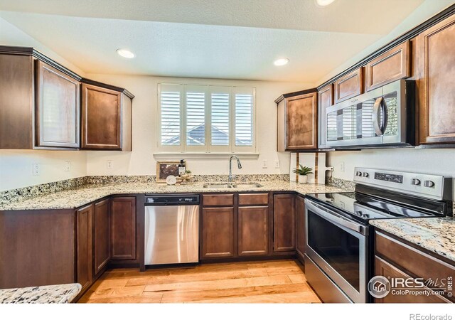 kitchen featuring light stone counters, sink, stainless steel appliances, and light hardwood / wood-style floors